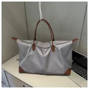 Large grey nylon travel tote bag with brown leather handles shown in a home office setting