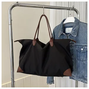 Large black nylon travel tote bag with brown leather handles hanging on a rack