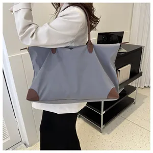 Large blue-gray travel tote bag carried by a model in a professional office environment.