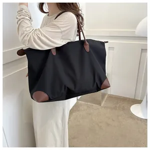 Side view of a large black travel tote bag with brown leather handles for women