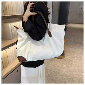 Woman carrying a large white travel tote bag with brown leather handles in a library setting.