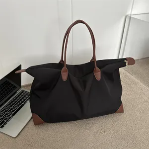 Large black nylon travel tote bag with brown leather handles placed next to a laptop