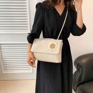 Bolso bandolera de paja color crema a la moda con detalle floral llevado por una modelo