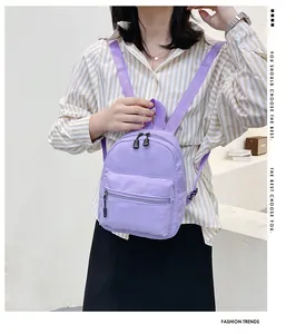 Model wearing a small purple nylon backpack with adjustable straps for school or travel.