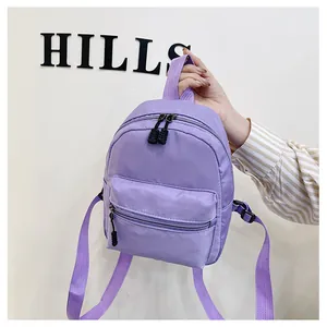 Close-up detail view of a stylish purple nylon mini backpack held against a white wall