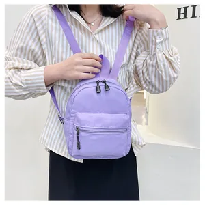 Close-up of a light purple nylon mini backpack worn by a model in a casual setting.