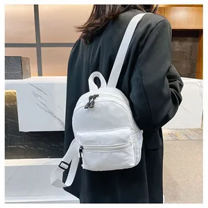 Back view of a minimalist white nylon mini backpack worn by a model in a black blazer