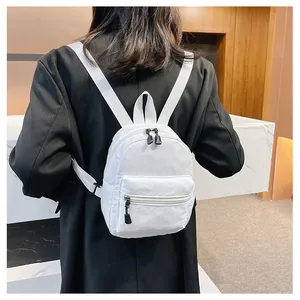 Back view of a woman wearing a minimalist white nylon mini backpack in a modern setting