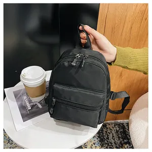 Compact black nylon backpack detail held by hand in a stylish lifestyle setting