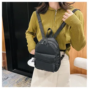 Back view of a model wearing a compact black nylon backpack with a zipper front pocket.