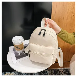 Close-up lifestyle view of a minimalist cream white nylon mini backpack on a white table