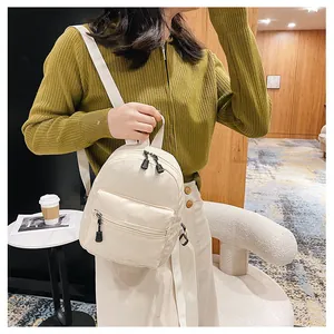 Close-up of a women's cream nylon mini backpack worn by a model in a modern cafe