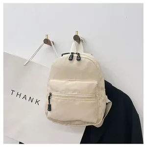 Lifestyle detail of a minimalist cream nylon mini backpack hanging on a hook