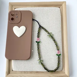 Detalle de cuentas de bambú verde y dije de tulipán rosa en una correa para teléfono.