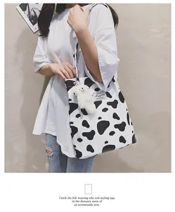 Vue détaillée d'un sac cabas en toile à motif vache avec un adorable pendentif ours.