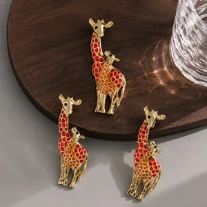 Close-up detail of three elegant gold-toned enamel giraffe brooches on a dark wooden base
