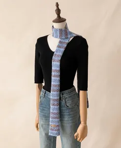 Detailweergave van een blauwe gebreide smalle sjaal met bruine patronen op een mannequin.