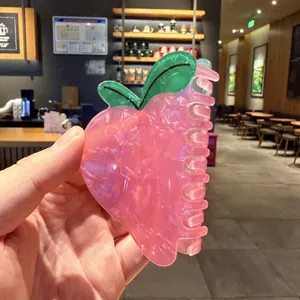Detalle de una linda pinza para el cabello en forma de melocotón rosa con hojas verdes