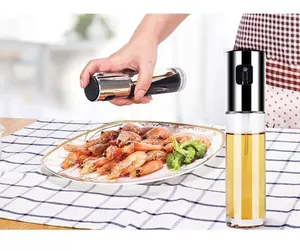 Professional action shot showing glass oil sprayer misting grilled shrimp on a ceramic plate.