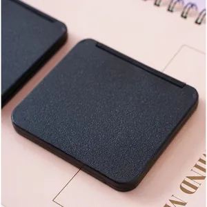 Close-up view of a sleek matte black foldable pocket mirror on a pink notebook