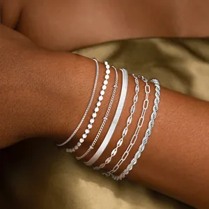 Détail de plusieurs bracelets argentés superposés sur un poignet, styles variés.