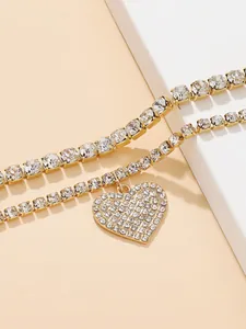Detailed close-up of gold tennis anklets with a sparkling rhinestone-paved heart charm.