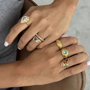 Primo piano di anelli dorati martellati con zirconi colorati scintillanti sulle dita.