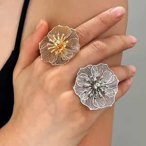 Eleganti grandi anelli floreali in filigrana traforata oro e argento su una mano.