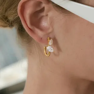 Detalle de un pendiente en forma de J de acero inoxidable dorado con dos circonitas