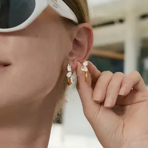 Primer plano de elegantes pendientes de acero dorado con cristalli de circonio blanco en la modelo