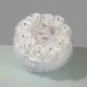 Close-up of white heart-shaped ring pillow decorated with satin roses and lace details