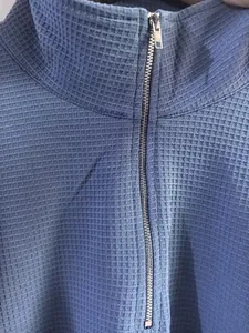 Close-up of waffle knit texture and metal zipper on blue stand-collar sweatshirt