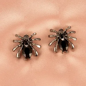 Nahaufnahme von gotischen Spinne Ohrsteckern mit schwarzen Strasssteinen auf rosa Satin