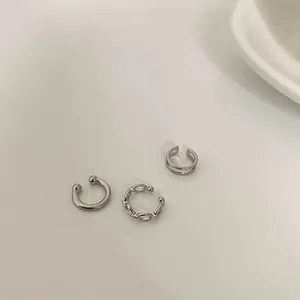 Close-up of three minimalist silver non-pierced geometric ear cuffs with hollow textures