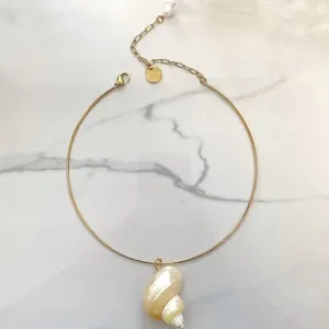 Detail van een gouden choker ketting met een natuurlijke schelphanger en witte parel.