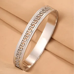 Close-up of a silver stainless steel bangle featuring a hollow Greek key pattern design