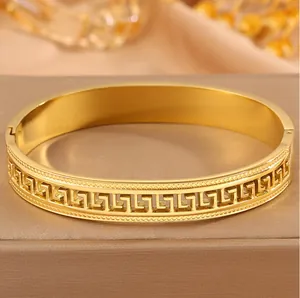 Close-up of gold titanium steel bangle with hollow Greek key pattern detail.