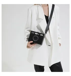 Creative black camera-shaped crossbody box bag shown on model wearing white blazer