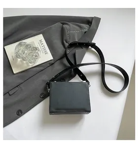 Minimalist black vintage box crossbody bag presented with a stylish gray blazer background