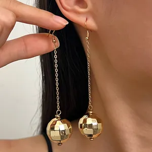 Dettaglio di orecchini a palla da discoteca dorati con sfera di metallo sfaccettata