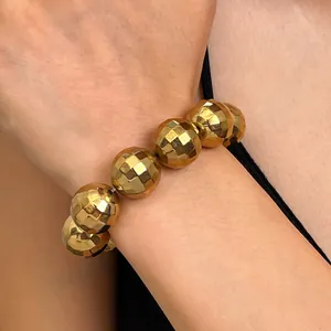 Dettaglio di un bracciale con sfere sfaccettate color oro al polso.