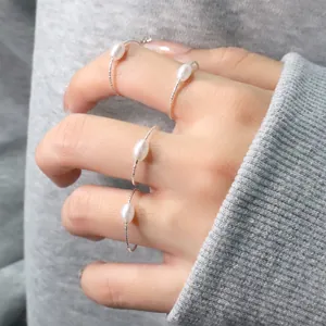 Detailansicht von minimalistischen Silberringen mit ovalen Perlen im Lagen-Look getragen.