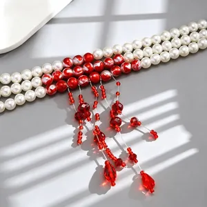 Detailed view of triple-strand pearl necklace with red beaded tassels and drop charms