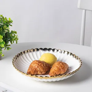 Close-up of elegant ceramic dinner plate with scalloped gold rim and croissants