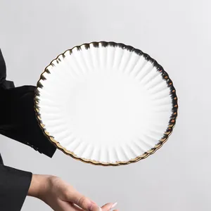 Elegant white ceramic dinner plate with gold scalloped edge detail held by a person