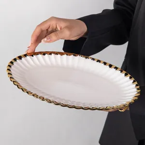 Close-up view of a luxury white ceramic oval plate featuring a gold and black scalloped rim