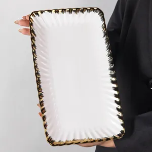 Detailed view of rectangular white ceramic plate with wavy texture and gold rim.