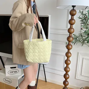 Eine weiche gelbe gesteppte Tragetasche mit Herzmuster, gehalten von einem Modell