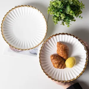 Elegant white ceramic dinner plates with gold scalloped rims and ribbed texture