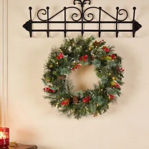 Detailansicht eines Weihnachtskranzes mit roten Beeren, Zapfen und warmen Lichterketten.